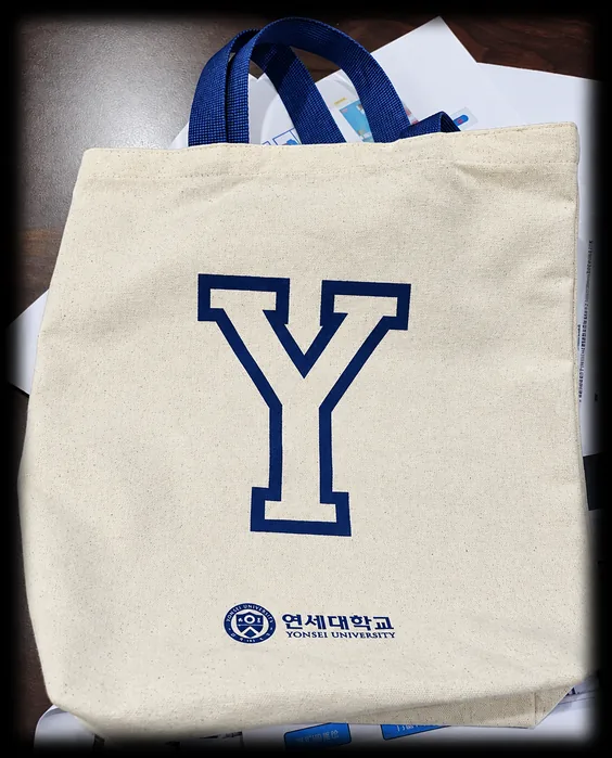 아이보리색 캔버스 에코백에 남색 Y 로고와 대학 마크를 인쇄한 사진